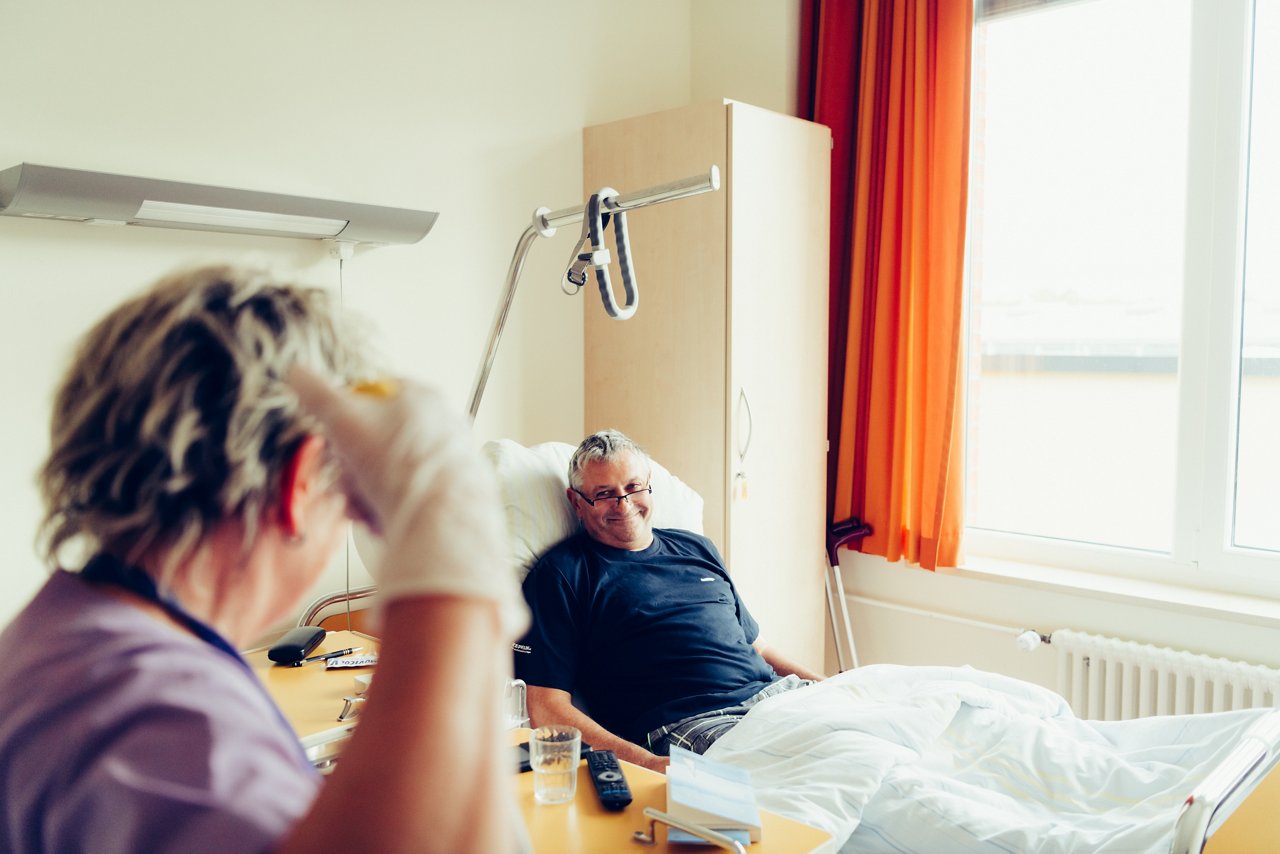 Patient im Krankenbett lächelt der Reinigungskraft zu, die das Krankenzimmer wischt