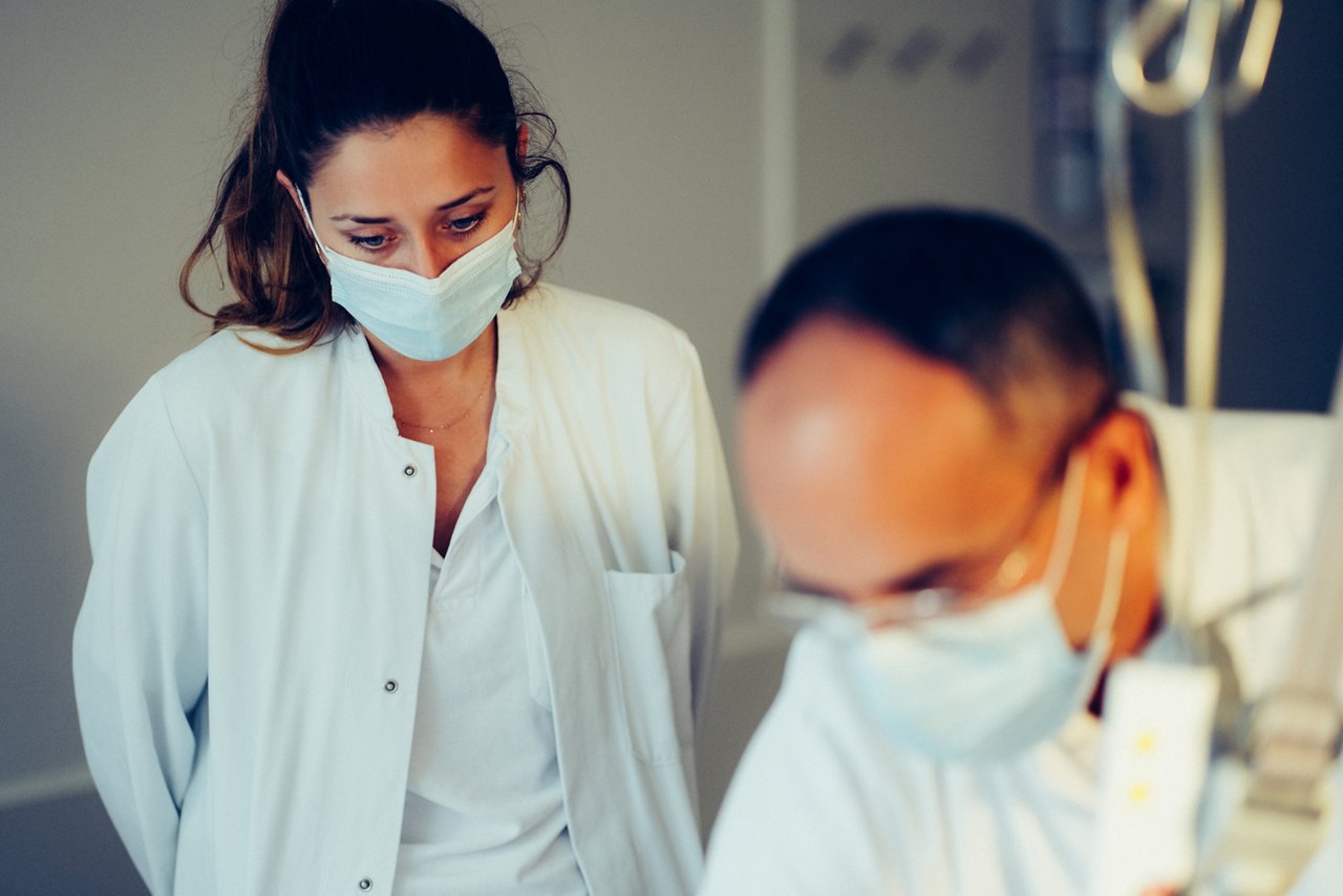 Arzt untersucht Patient:in, der:die nicht zu sehen ist, eine weitere Ärztin schaut zu