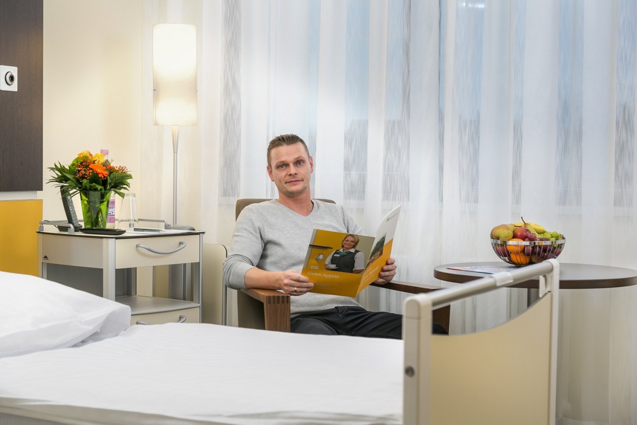 Patient sitzt auf einem Sessel im Wahlleistungszimmer und liest eine Broschüre