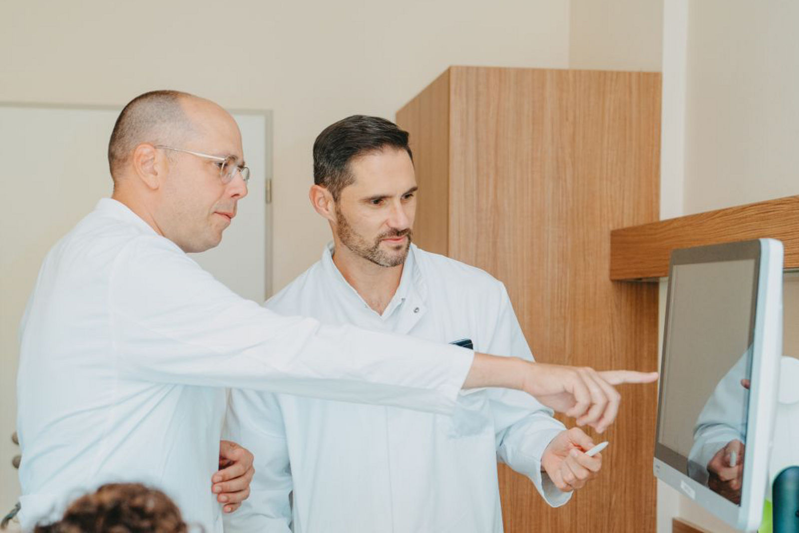 Visite im Patientenzimmer, Patientin sitzt auf Bett und Ärzte besprechen ihre Akte 