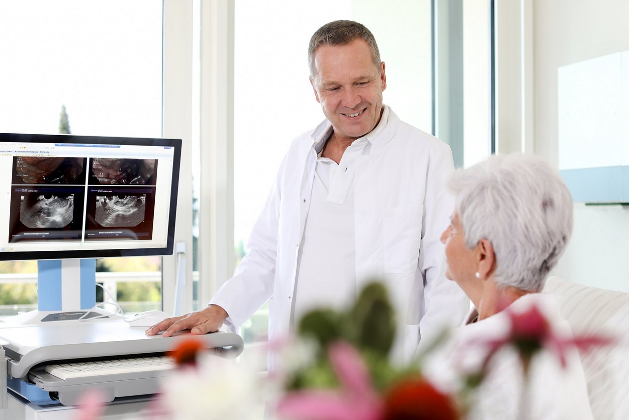 Im Patientenzimmer mit Dokumentationswagen - Gespräch zwischen Patientin und seinem Arzt während der Visite