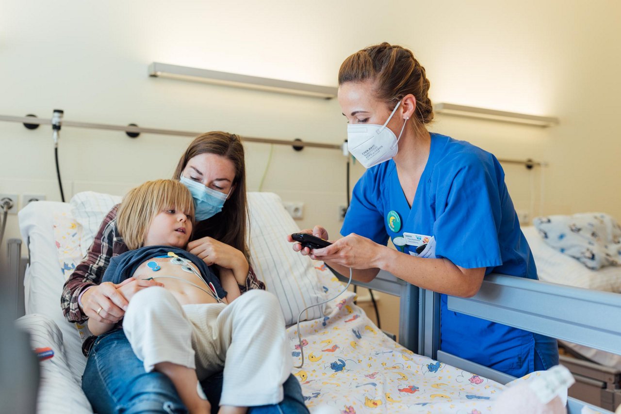 Gesundheits- und Kinderkrankenpflegekraft am Bett mit Mutter und Kind