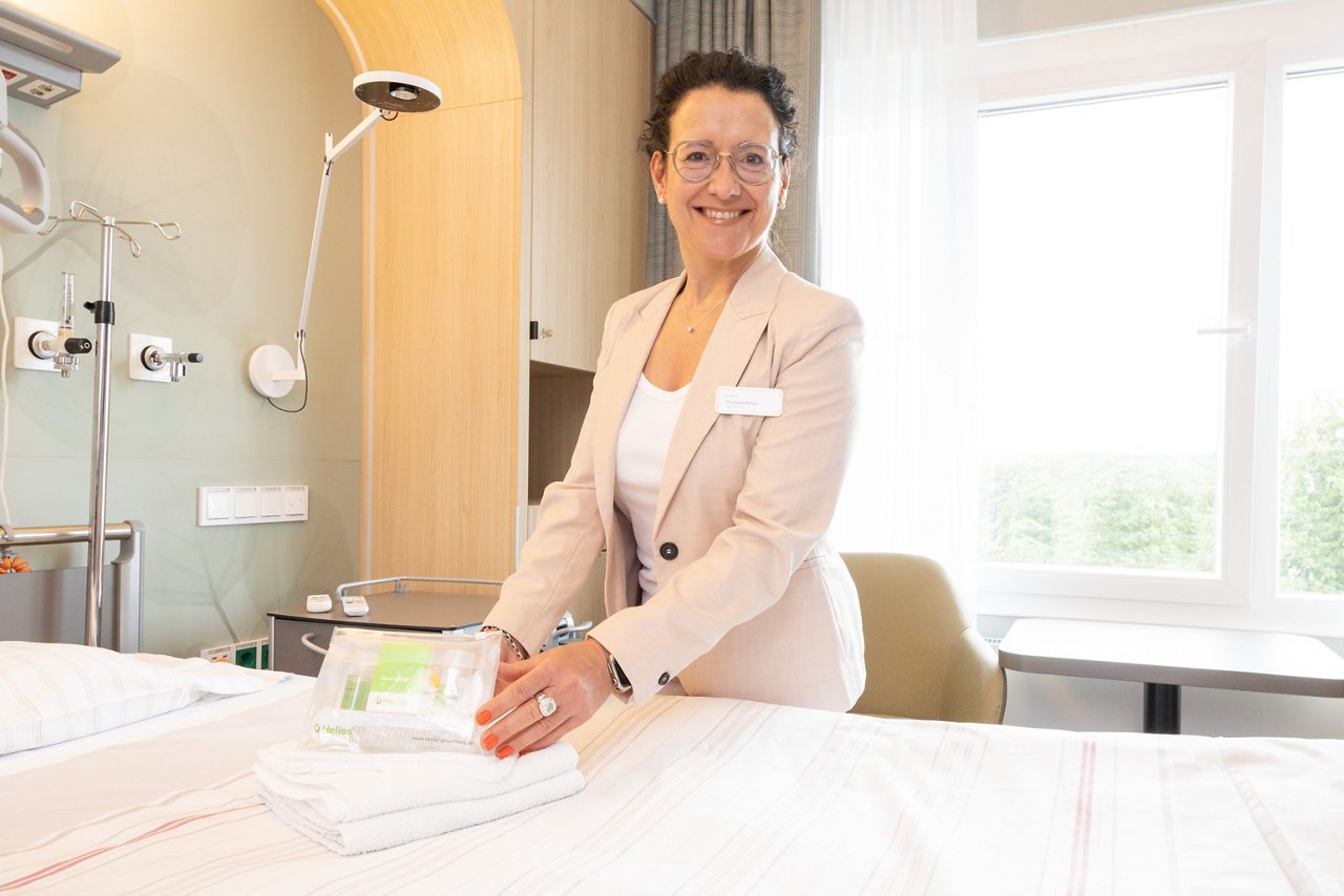 Wahlleistungsmanagerin steht am Patientenbett in Privatklinikzimmer mit Kosmetiktasche