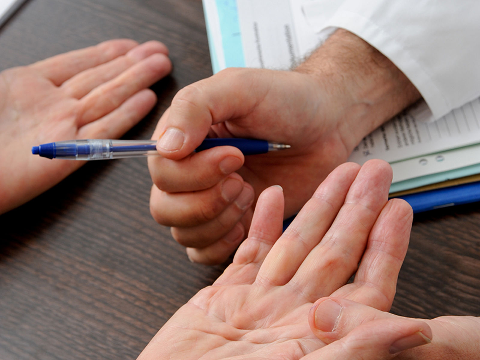 Arzt hält Patienten-Hand in der Hand mit Kugelschreiber zur Erklärung Handchirurgie