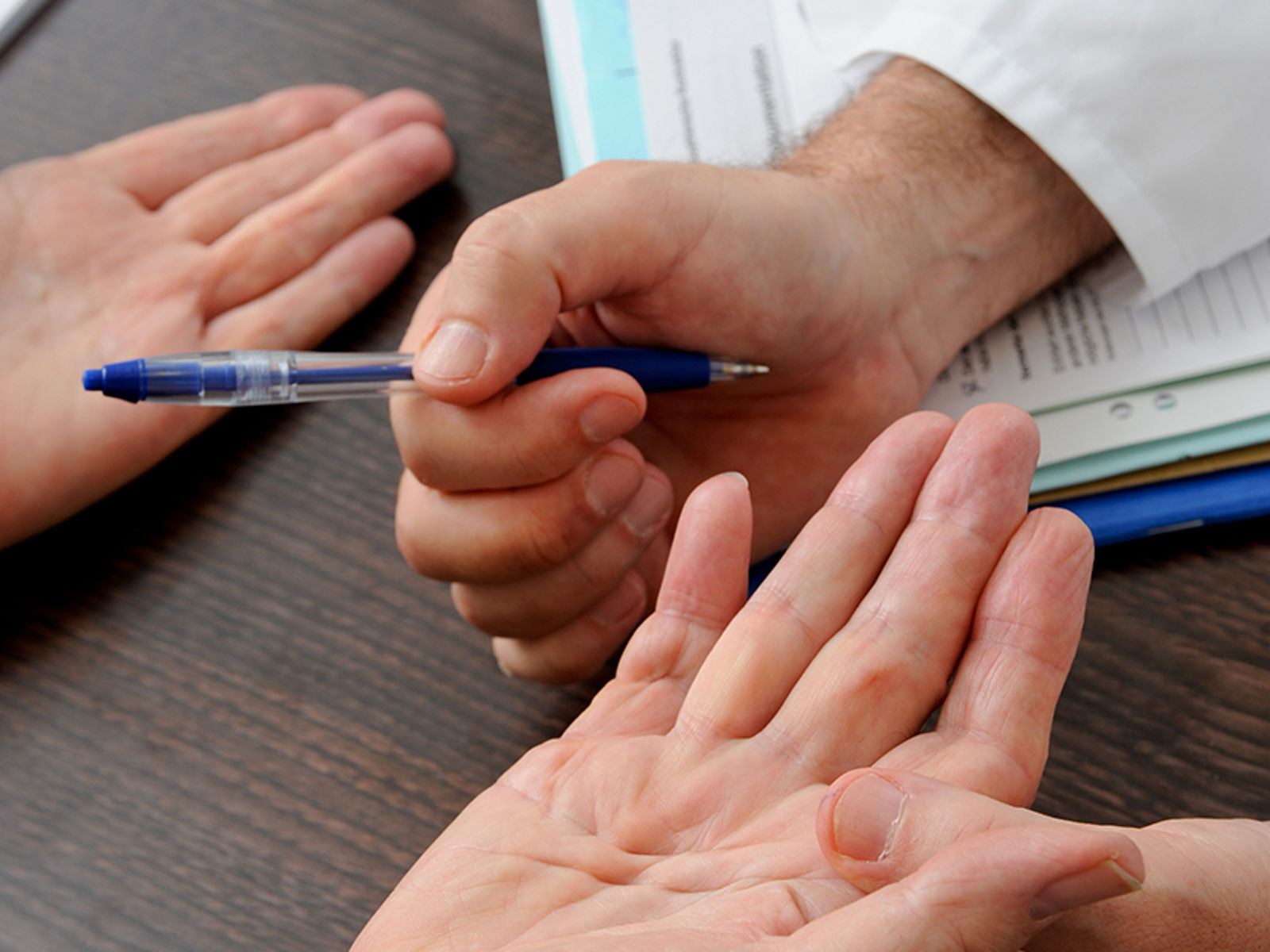 Arzt hält Patienten-Hand in der Hand mit Kugelschreiber zur Erklärung Handchirurgie
