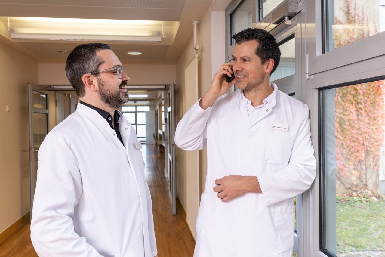 Ärzte der Kardiologie stehen auf Stationsflur und telefonieren