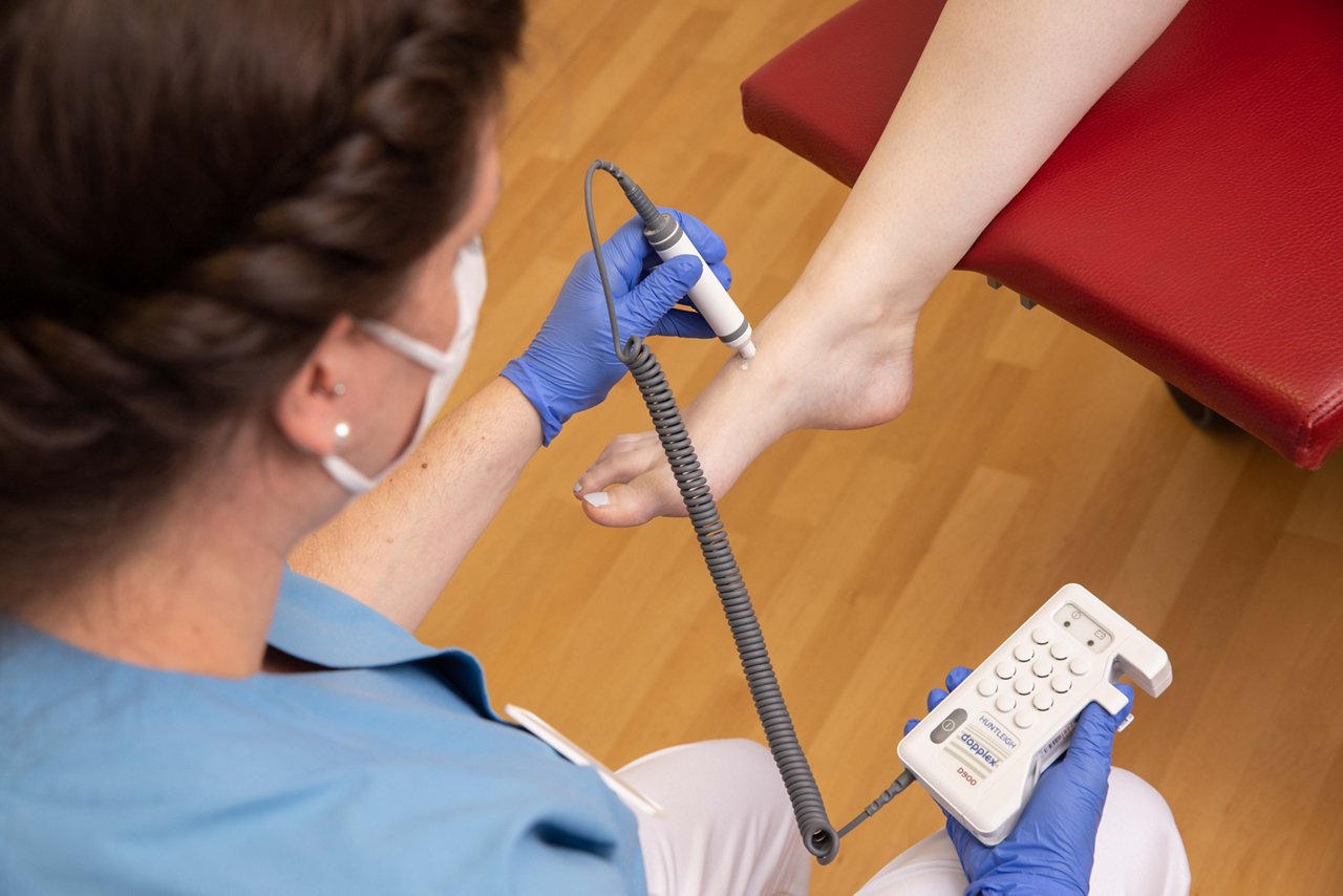 Pflegerin misst mittels Dopplersonografie am Fuß einer Patientin Gefäße