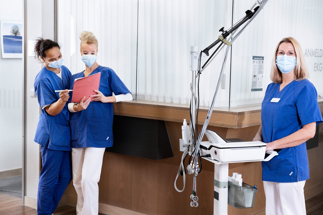 Drei MFAs stehen auf dem Flur mit Maske und dokumentieren. 