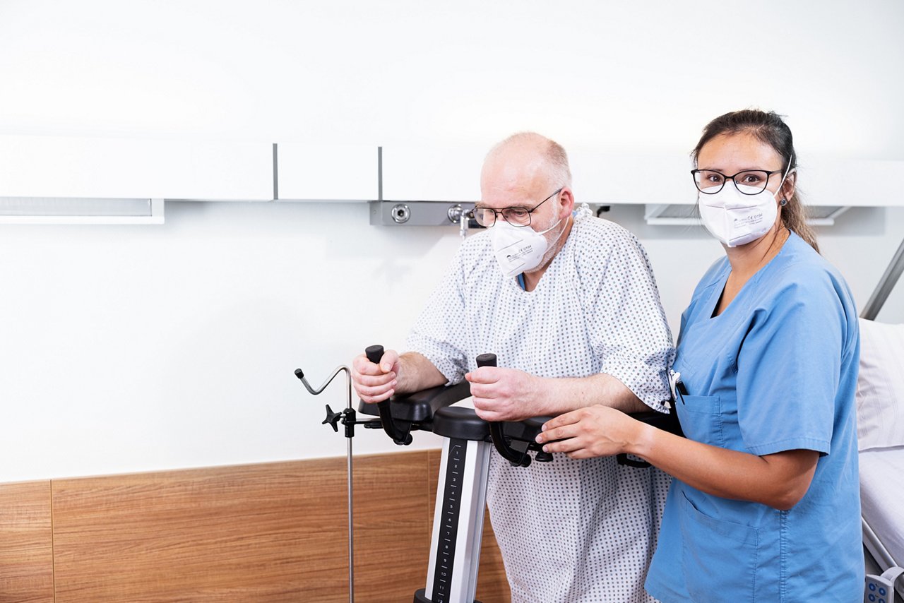 Pflegerin im Patientenzimmer und FFP2-Maske stützt Patient am Gehwagen