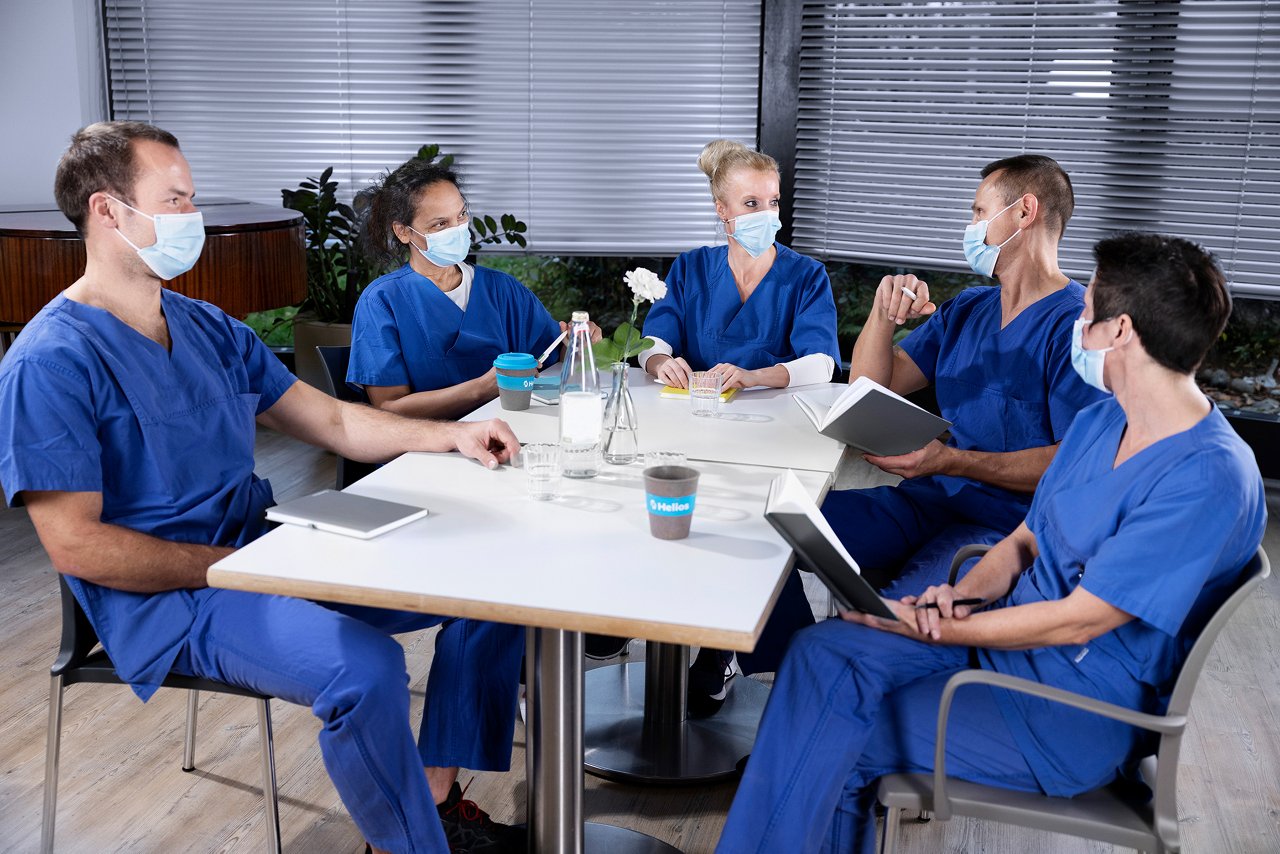 Pflegerinnen und Pfleger bei Teamsitzung mit Masken im Besprechungsraum 