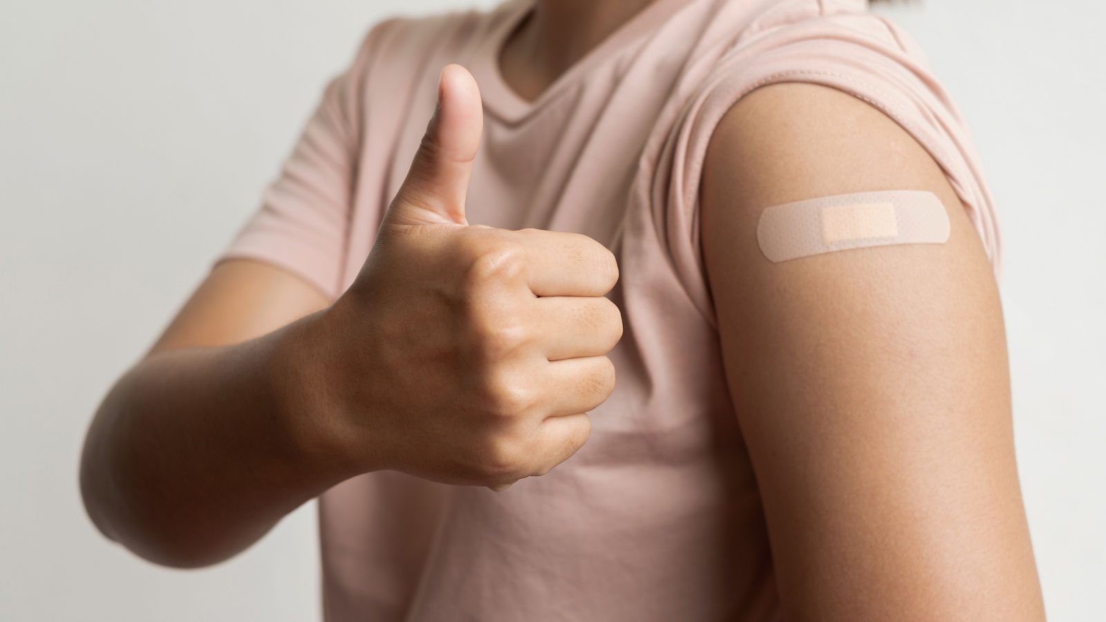Asian woman shows plaster on her shoulder after being vaccinated against Covid-19. Coronavirus vaccination campaign concept
