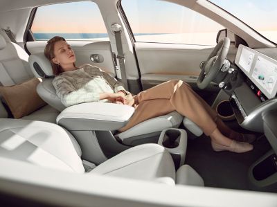 A woman resting in the reclined passenger seat insider her Hyundai IONIQ 5 electric CUV.