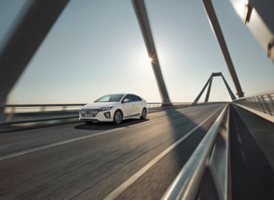 The new Hyundai Kona in Surfy Blue from the side driving over a bridge.