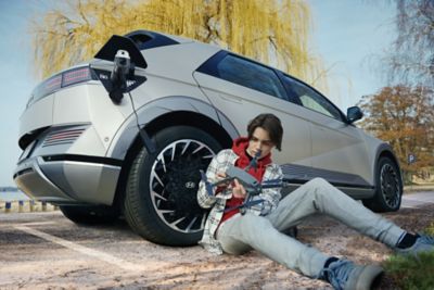 Adolescent rechargeant son drone en le branchant au CUV électrique Hyundai IONIQ 5 stationné sur la plage.