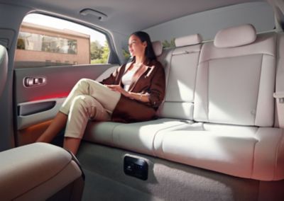 Femme assise à l’arrière de la berline 100 % électrique Hyundai IONIQ 6 avec éclairage d’ambiance rouge.
