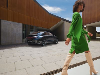 Geparkeerde Hyundai IONIQ 6, met erlangs lopende vrouw in groen.