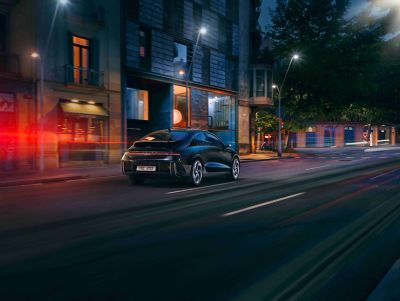 The Hyundai IONIQ 6 pictured from the side driving down a city street at night.