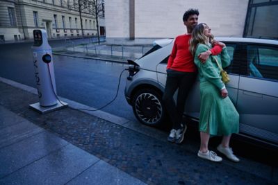 Un homme et une femme s’enlaçant à côté de l’IONIQ 5 qui est branché pour la recharge.