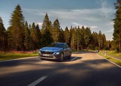 Imagen del nuevo Hyundai KONA en color Surfy Blue pasando por una carretera en el campo.