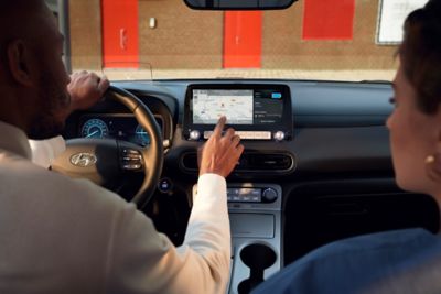 Ein Mann sitzt am Steuer des KONA Elektro und bedient mit der rechten Hand den 10,25-Zoll-Touchscreen.