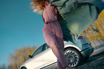 A woman dancing in front of an Hyundai IONIQ 5 with is parked in the nature.