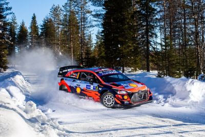 Hyundai i20 Coupe WRC driving through a mass of snow spraying both sides.