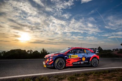 The new Hyundai 2022 i20 N WRC Rally1 in front of a sunset on the race track.
