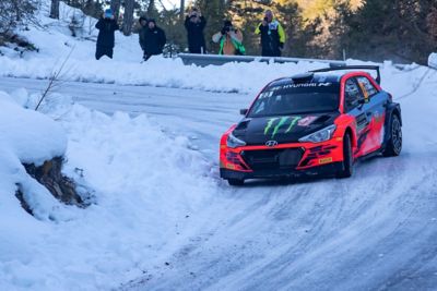 Voiture de rallye customer racing Hyundai Motorsport i20 R5 en action sur une route de montagne enneigée.