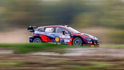 The Hyundai i20 Coupe WRC speeding down a road during a rally.