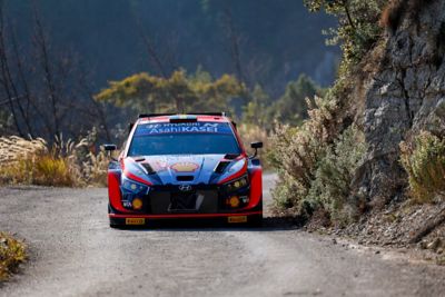 The Hyundai i20 N WRC rally race car driving fast on a panoramic route.