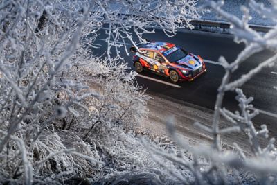Motor sport driver Thierry Neuville's Hyundai i20 WRC speeding down a country road in winter. 