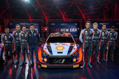 The Hyundai Motorsport race drivers standing next to the new 2022 i20 N WRC Rally1.