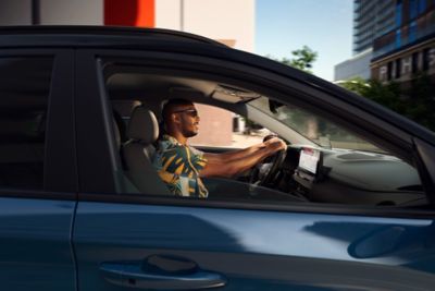 Blick durch das Beifahrerfenster des Hyundai KONA Elektro auf einen Mann mit Sonnenbrille am Steuer des Fahrzeugs.