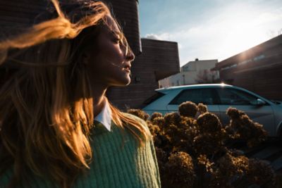 Une femme debout, au soleil à côté du Hyundai IONIQ 5 électrique CUV.