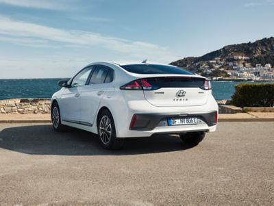 The Hyundai IONIQ Electric in a parking lot next to the sea pictured from the rear.
