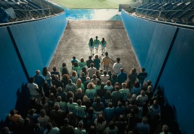 A crowd of football fans walking toward the pitch through a stadium tunnel.