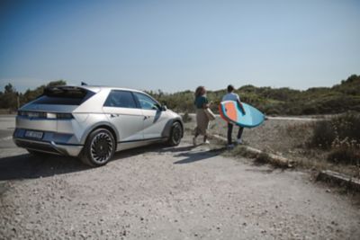 Hyundai IONIQ 5 EV zaparkovaný na pláži a dva surfaři vystupující z vozu.