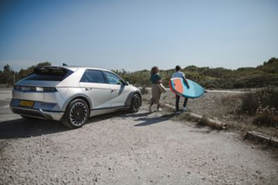 The Hyundai IONIQ 5 EV parked at a beach parking lot with two surfers next to it.