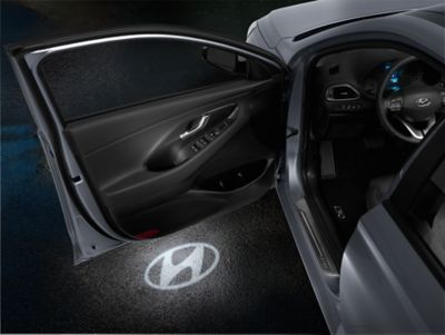 Rzutniki LED w drzwiach Hyundaia i30 Fastback wyświetlają logo Hyundai na podłożu.