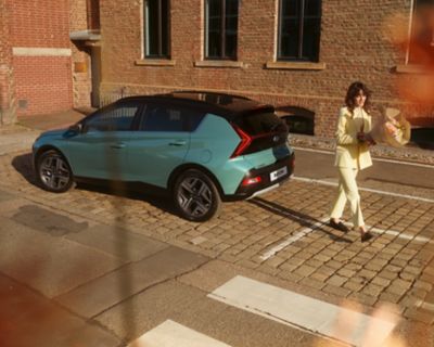 Woman in yellow walking away from the parked all-new Hyundai BAYON compact crossover SUV.​
