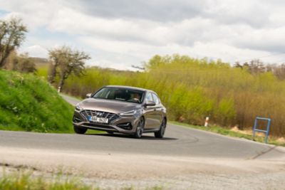 Hyundai i30 Fastback na okresní silnici za příjemného počasí.