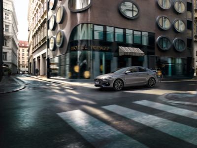 The Hyundai i30 Fastback with the accessories tow bar and bike carrier driving on a city road.