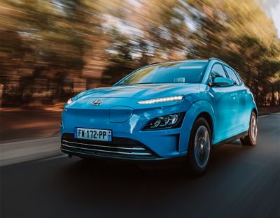 The Hyundai KONA Electric pictured from the front driving down a country road.