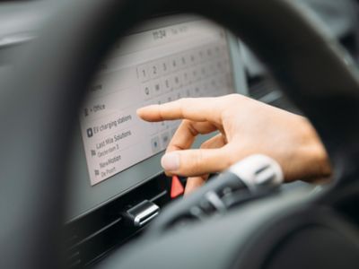 A driver of a Hyundai electric vehicle looking for a charging station on the display.