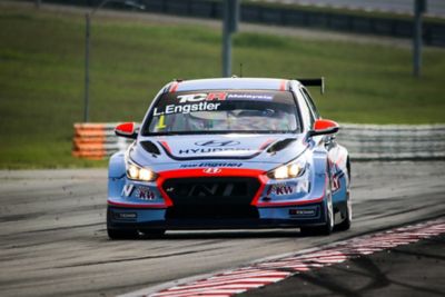  A picture of Hyundai Motorsport’s i30 Veloster N TCR in action on a racetrack shown from the front.	