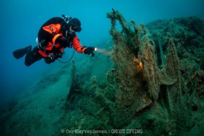 Buceador bajo el agua con una linterna, inspeccionando el lecho marino en busca de redes de pesca