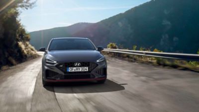 The Hyundai i30 N driving in a hilly set in the colour Dark Knight Pearl.