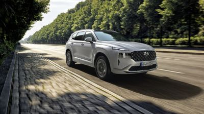 El nuevo Hyundai SANTA FE Híbrido Enchufable de 7 plazas aparcado frente a una casa.