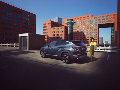 The all-new Hyundai Tucson compact SUV pictured from the rear parked near a waterfront skyline.