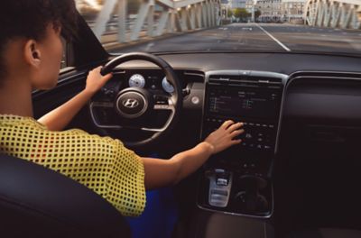 Zicht op het interieur van de Hyundai TUCSON SUV en de bestuurder die het touchscreen gebruikt.
